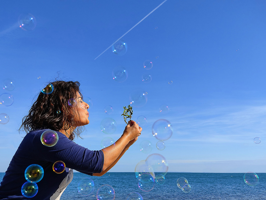 Young woman blowing leaves in front of the sea and soap bubbles around her