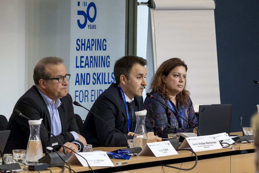 Three people in a panel with a banner at the background